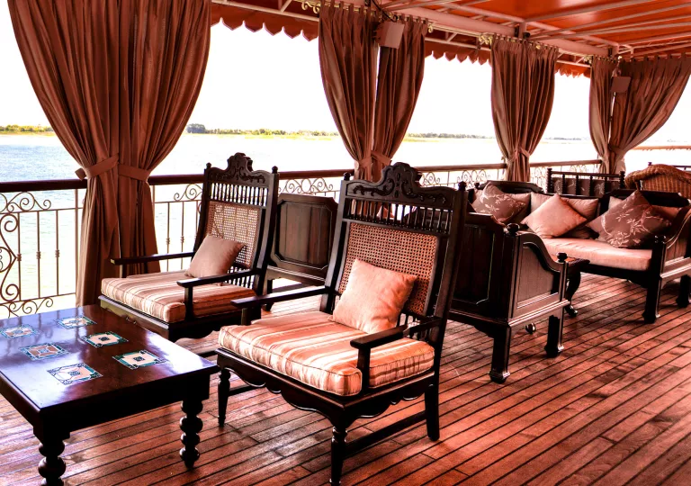 Wooden patio with large, red curtains and cushioned chairs looking out towards a lake