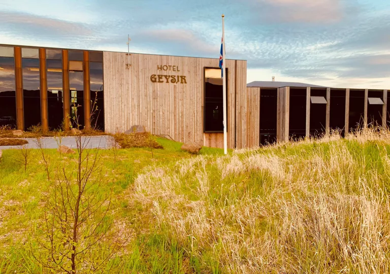 Exterior view of hotel building with a flag pole and grass field in front