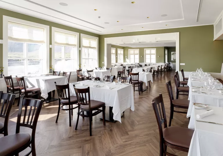 Dining hall in a green room, white white table cloths and large windows