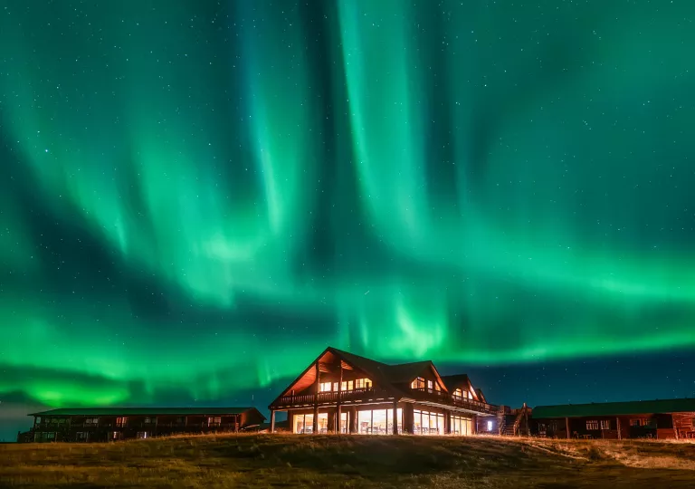 Illuminated wooden lodge in the middle of a valley, with an aurora in the sky