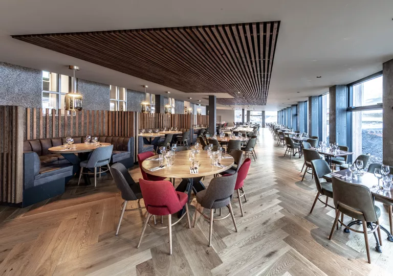 Dining hall with wooden fixtures on the ceiling, and red and black chairs surrounding each table