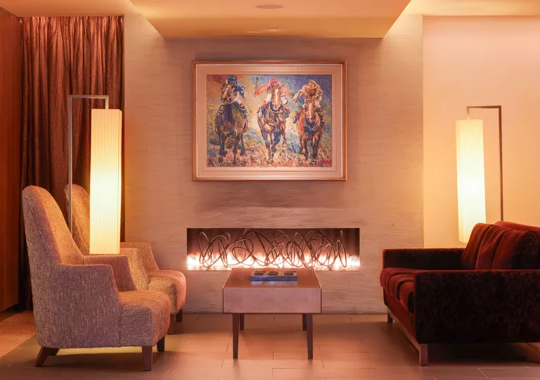 Two cushioned chairs in front of a fireplace with a painting of horse riding above