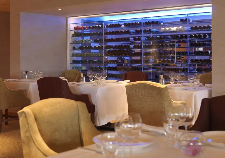 Dining area with wine glasses and a glass case full of wine bottles in the background