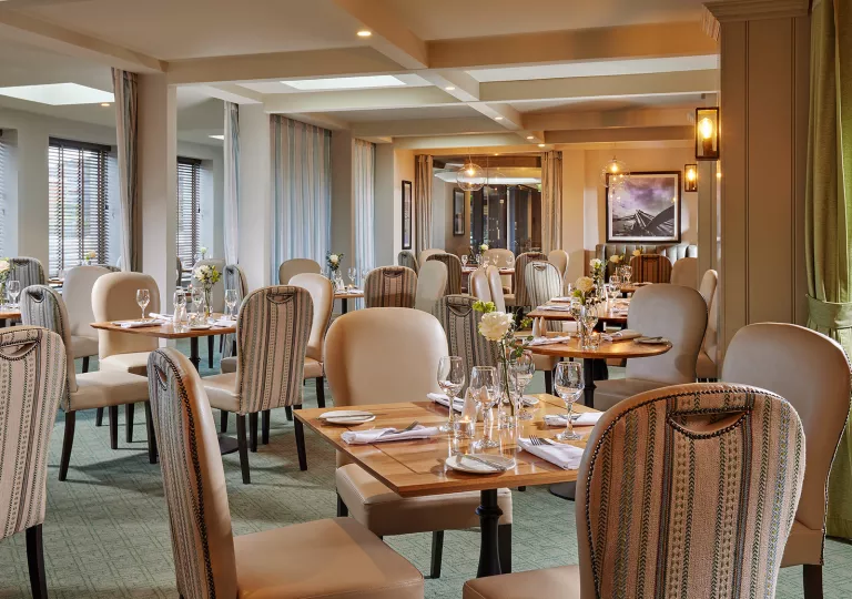 Indoor dining hall with tan chairs and wooden tables, with wine glasses on each table