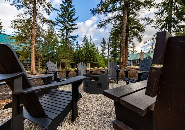 Black reclining chairs surrounding a black fire pit in the middle of a forest