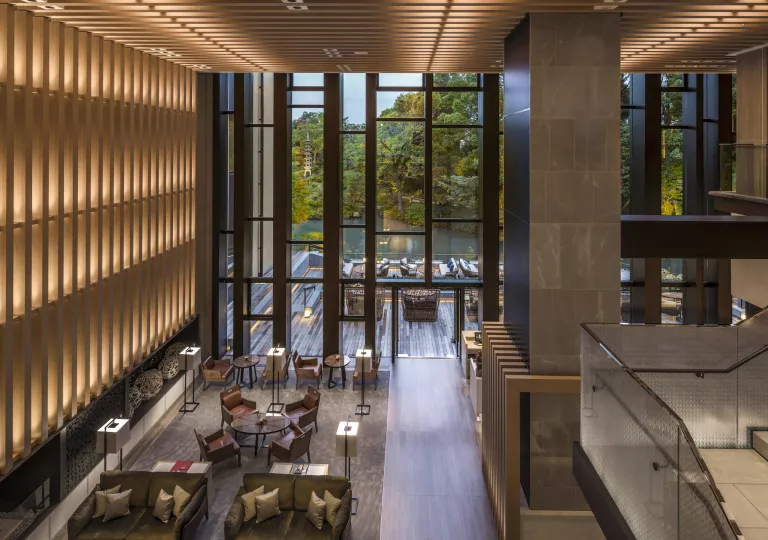 Indoor hotel lobby with large wooden panels on the walls and large windows looking out to the forest