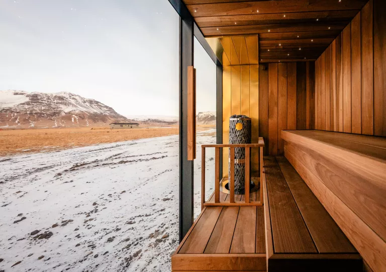 Wooden sauna with large, glass walls viewing out to a snowy mountain