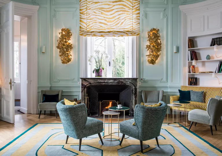 Two blue, cushioned chairs in front of a fireplace in a lobby