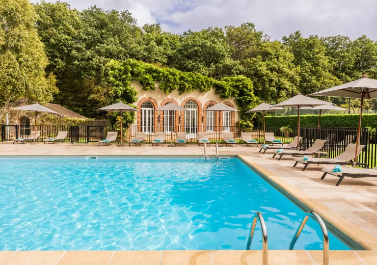 Outdoor pool with a tan building covered in plants, with tall trees in the background