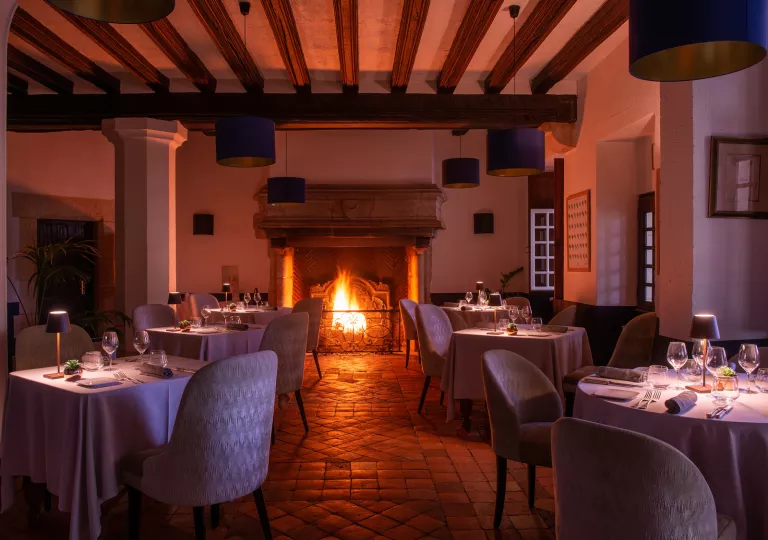 Indoor dining hall with small lamps on each table, and a fireplace in the back