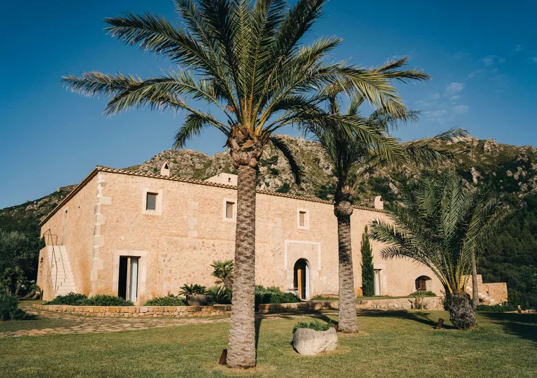 Yellow, stone building surrounded by palm trees, with a mountain in the background