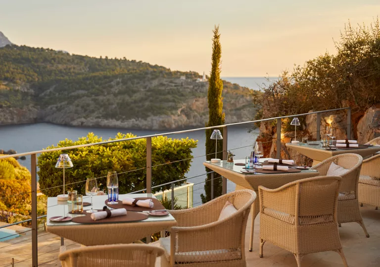 Outdoor patio with woven chairs and glass tables, looking out to a lake