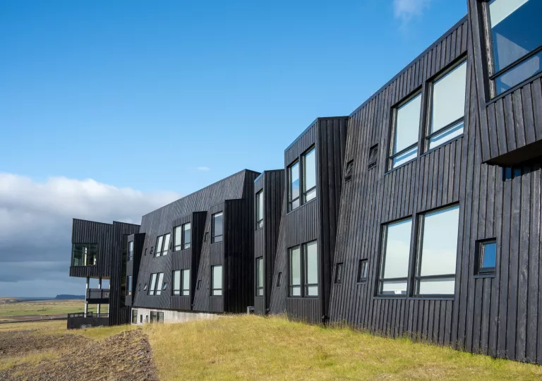 Exterior view of black, wooden building with large windows in the middle of a grass valley
