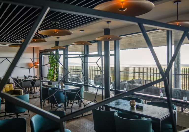 Indoor dining area with stone tables and green, cushioned chairs with large windows