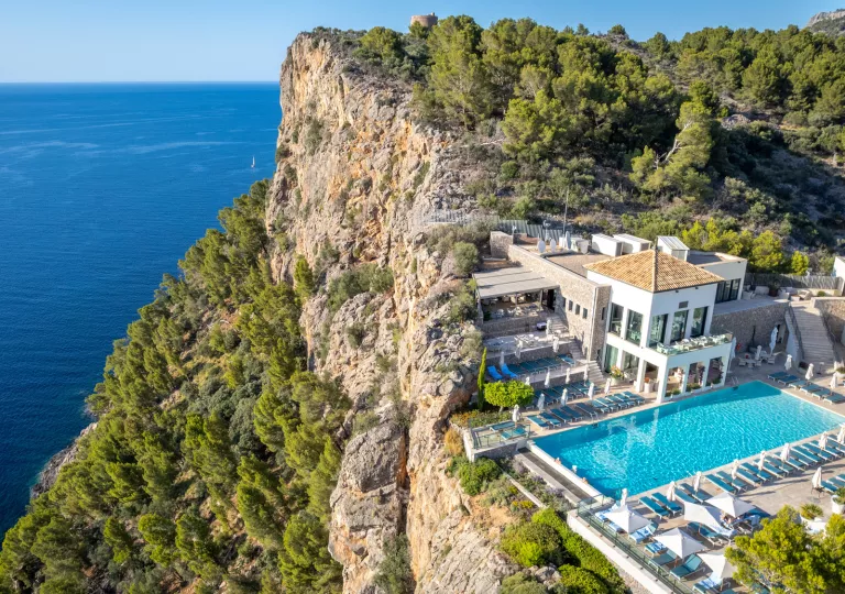Rocky, tree-filled cliff with a white hotel building and outdoor pool