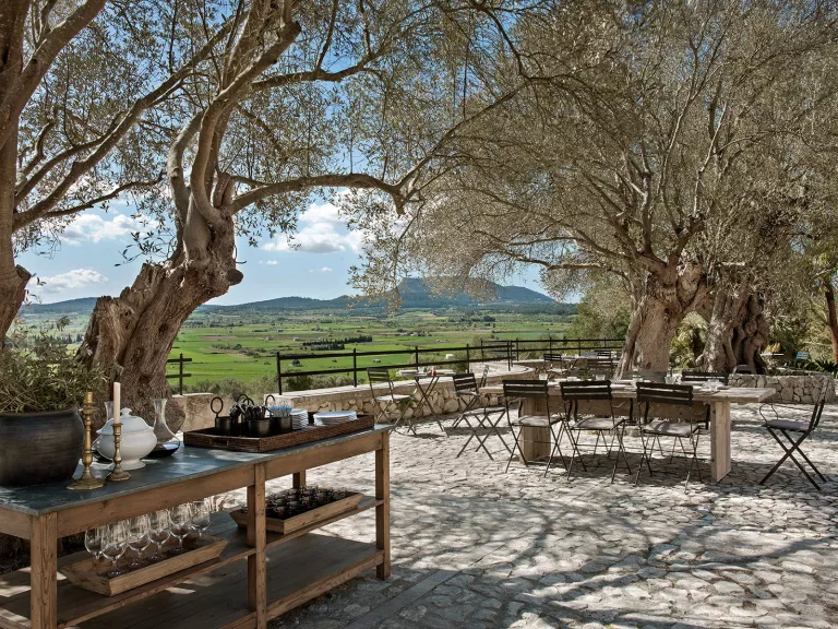 Outdoor seating area with wooden chairs and tables, with a large grass valley in the background