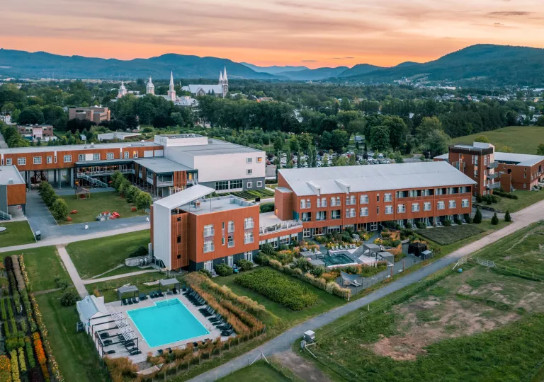 Exterior view of orange and gray building complex, with tall trees and giant churches in the background