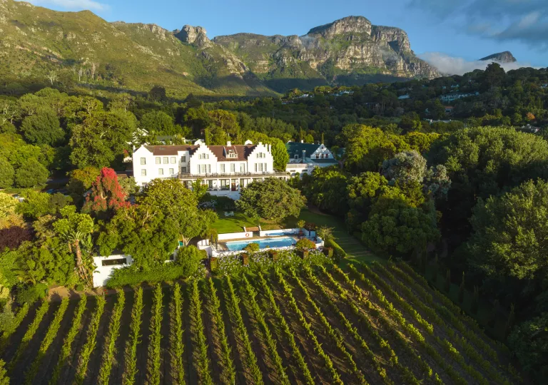 Exterior view of a white ad brown building, with a crop field and trees surrounding it