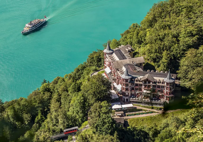 Sky view of  castle-like hotel building surrounded by trees and a cruise boat in the ocean on the left