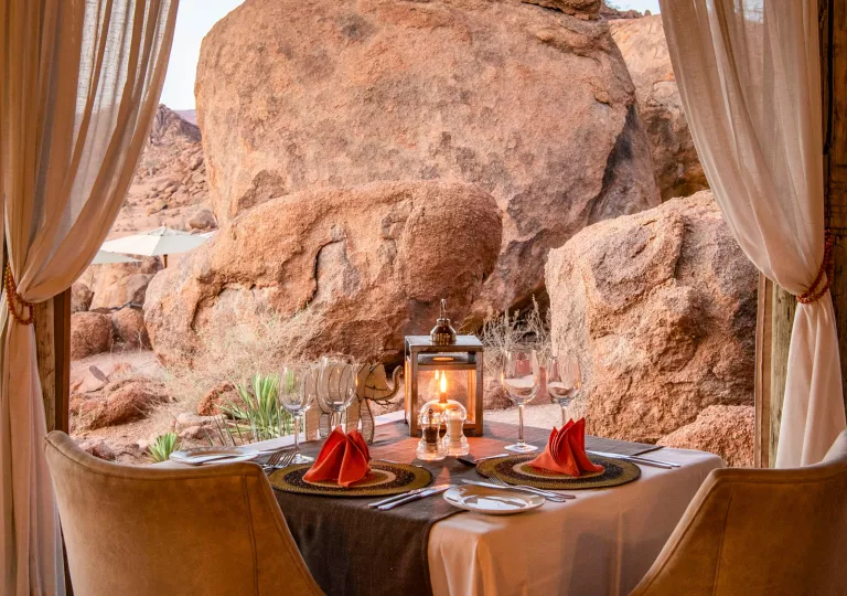 Dining table with wine glasses and a lantern with giant boulders in the background
