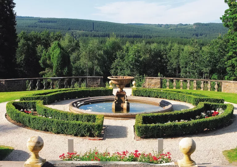 Circular fountain surrounded by trimmed hedges and flowers