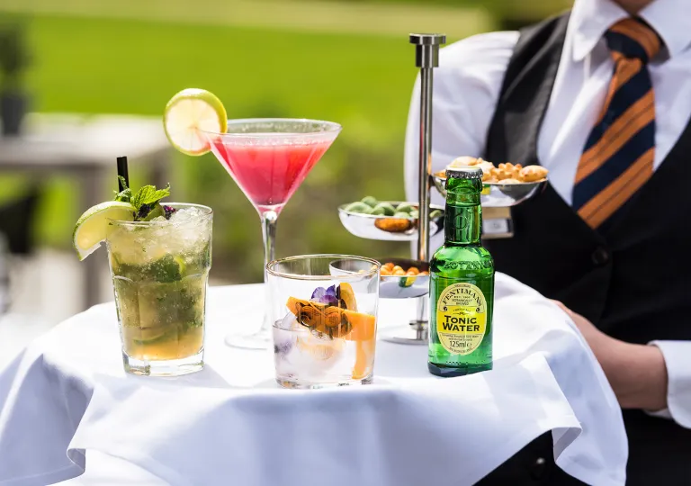 Waiter holding a tray full of mixed drinks and a bottle of tonic water