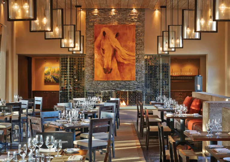 Indoor dining hall with wine glasses on the tables with a large painting of a horse on the wall