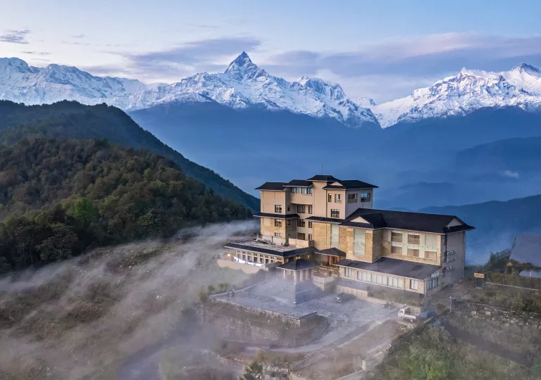 Hotel on top a hill surrounded by fog with mountains in the back