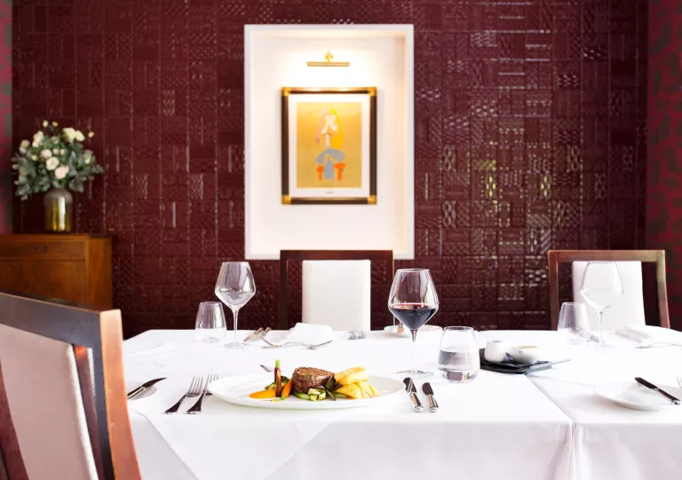 Dining table in a red room, with glasses of wine and a plate of food on the table