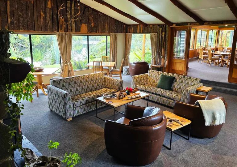 Large room in a wooden lodge with cushioned sofas and a dining table in the back
