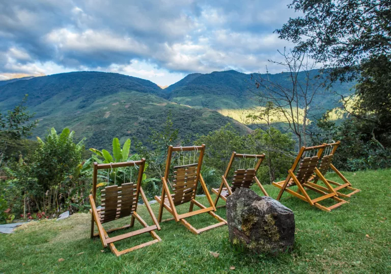 % wooden reclining chairs on a hill, looking out to grassy, tree-covered hills