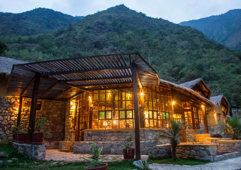 Exterior view of illuminated stone building, with a tall grass mountain in the background
