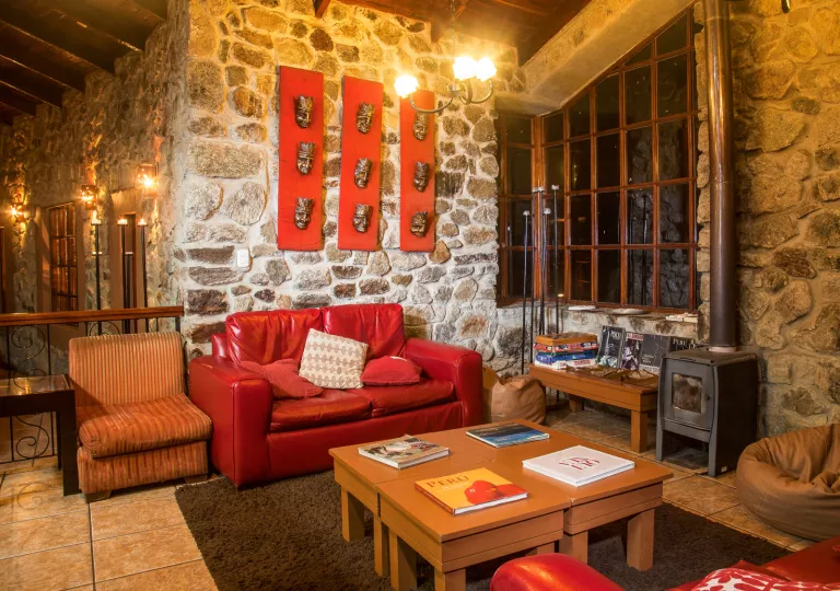 Stone-walled room with masks hanging on the wall, with a red couch in front of a furnace