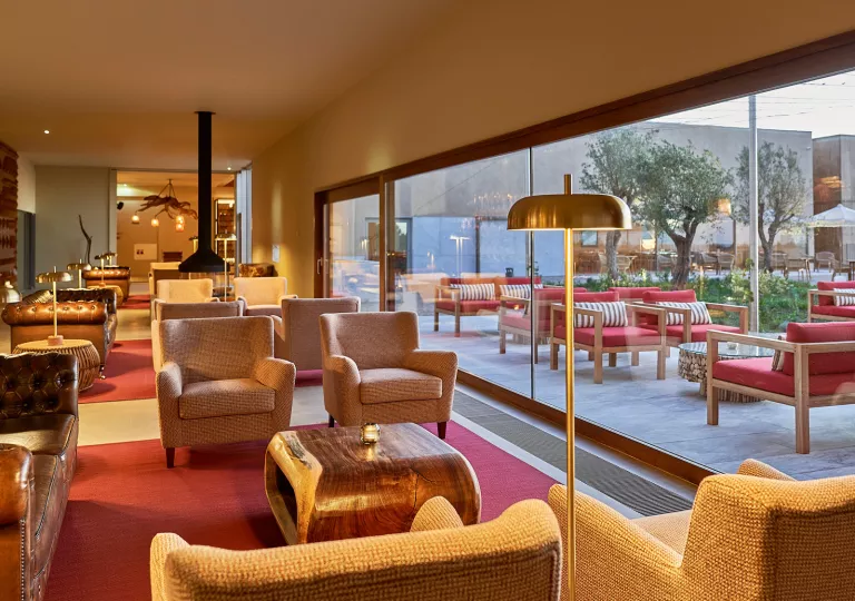 Indoor lounge area with cushioned chairs and large windows showing an outdoor patio