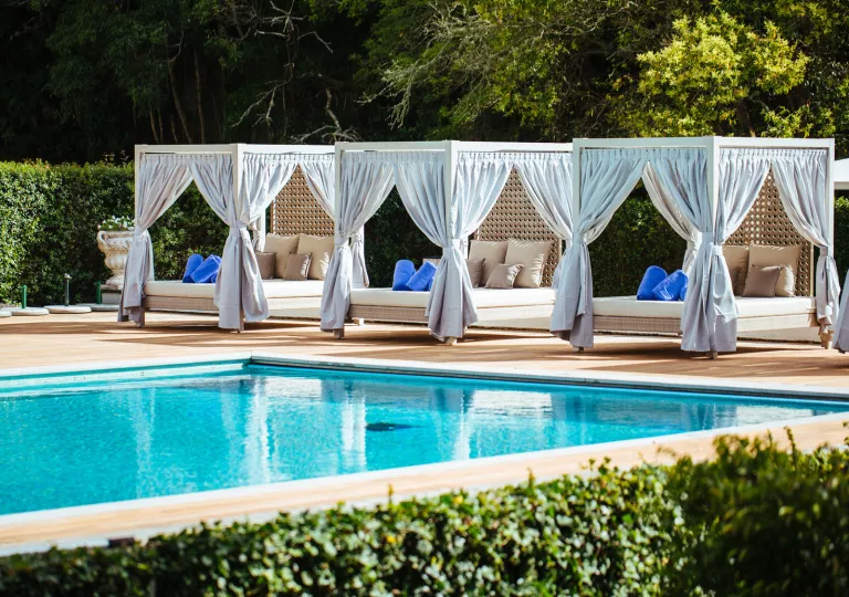 Outdoor pool with beds with large curtains surrounding the pool