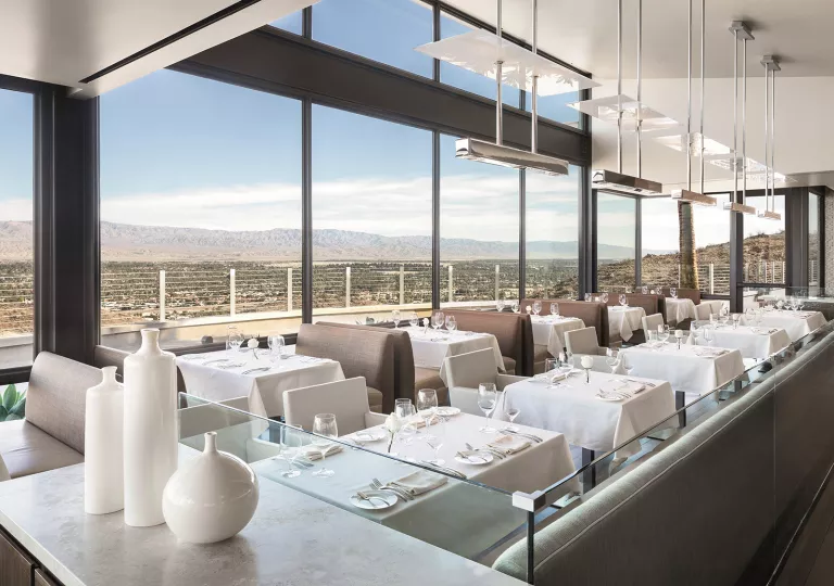 Indoor dining area with white tables and booths, looking out to large windows