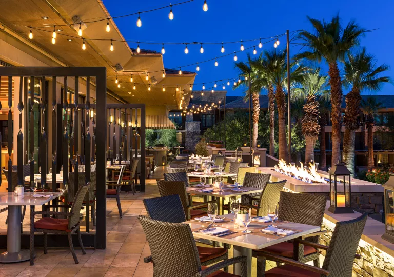 Outdoor dining area with string lights and palm trees to the right