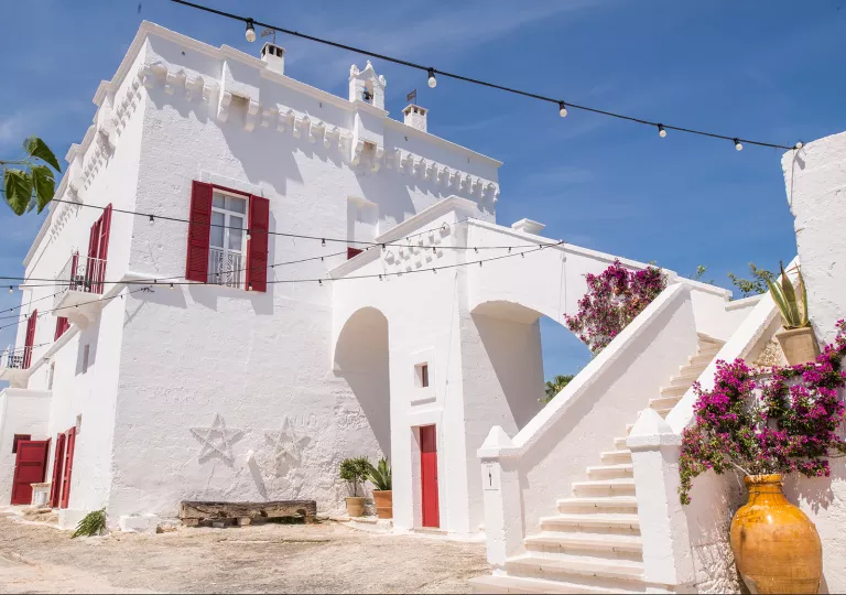 White stone building with red windows and doors, with a stairway on the right