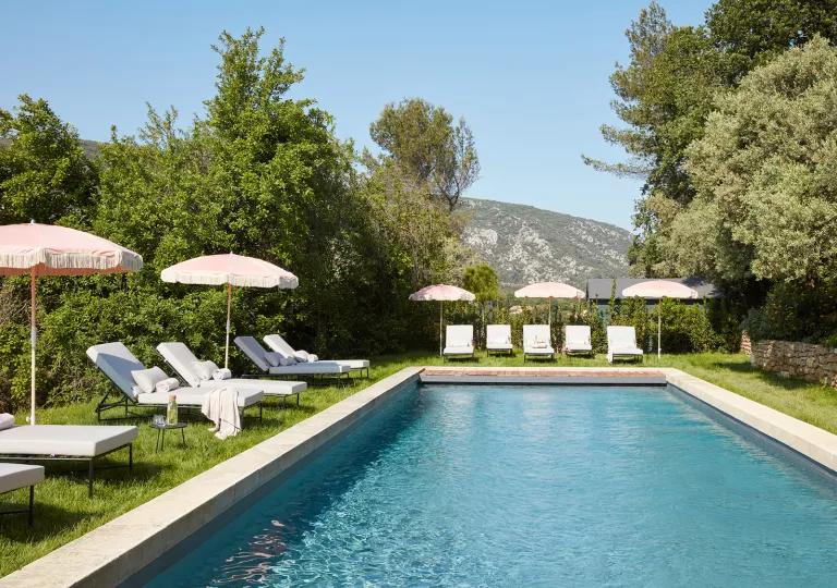 Outdoor pool surrounded by reclining chairs and umbrellas, with mountains in the distance