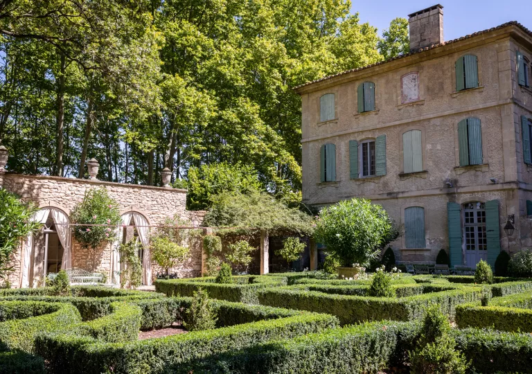 Outdoor garden with trimmed bushed next to a stone building