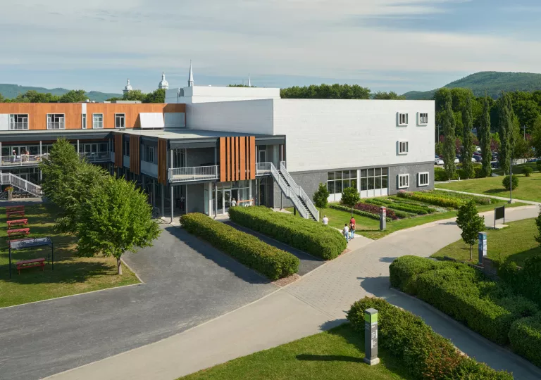 Exterior view of a gray stone building, with wooden accents and trimmed bushes in the front