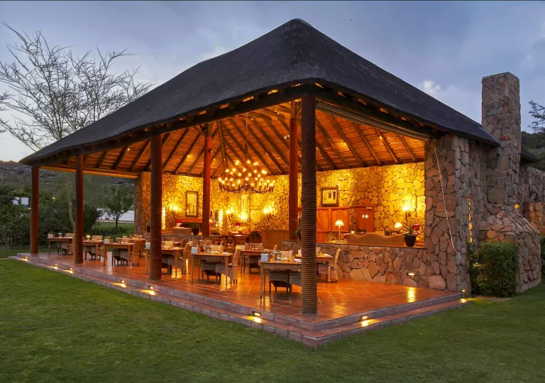 Outdoor, open dining patio with a chandelier, surrounded by a grassy area