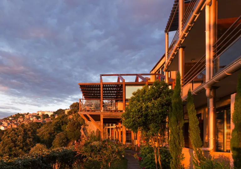 Exterior view of metal and wooden building, surrounded by trees in the sunset