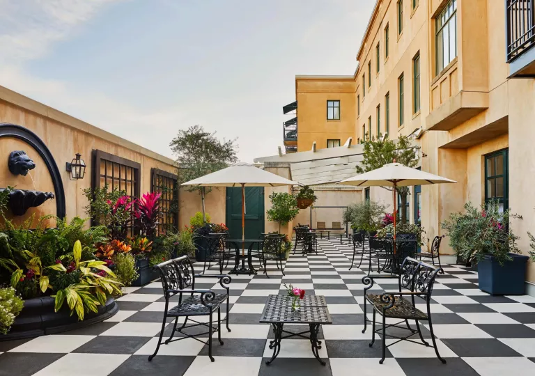 Outdoor patio with black and white checkered flooring, large plants and yellows buildings surrounding