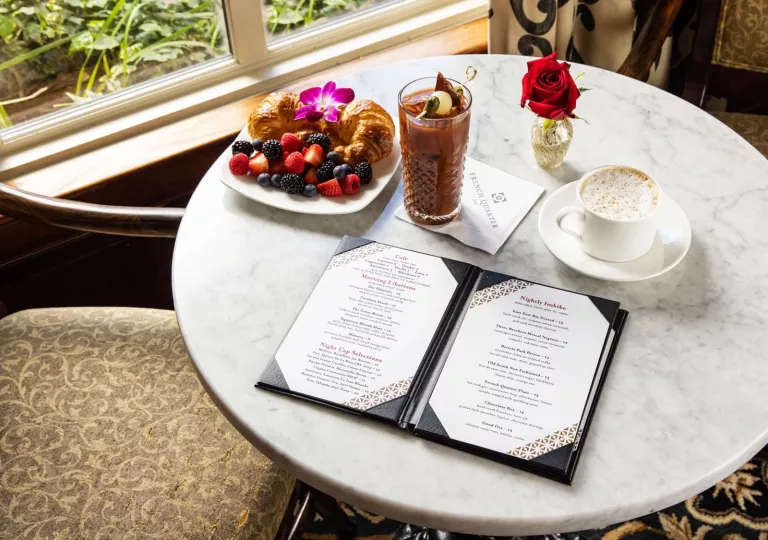 Circular, marble table with an open menu, a cup of coffee and a plate of pastries and fruits