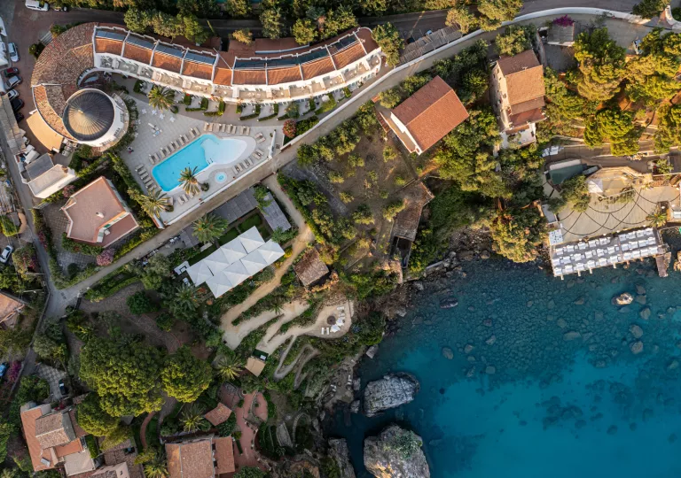 Sky view of white and tan buildings with an outdoor pool next to the shore of an ocean