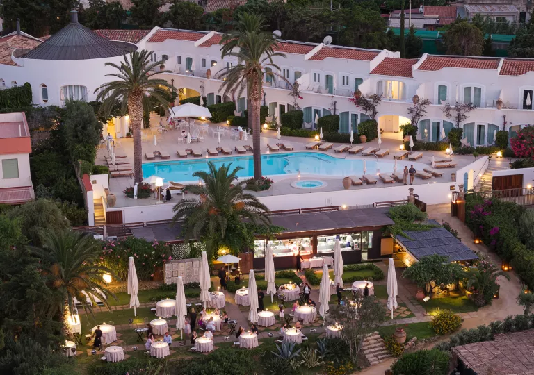 Sky view of white and tan buildings with an outdoor pool and tall palm trees