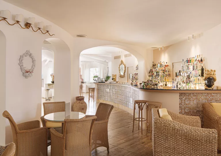 Bar and lounge with white walls, tiles on the bar, and woven chars around each table