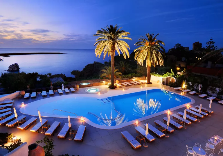 Outdoor pool with palm trees illuminated by lights
