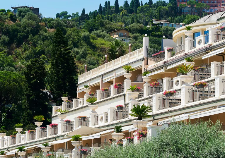 White hotel building with outdoor balconies, covered with pink and red flowers
